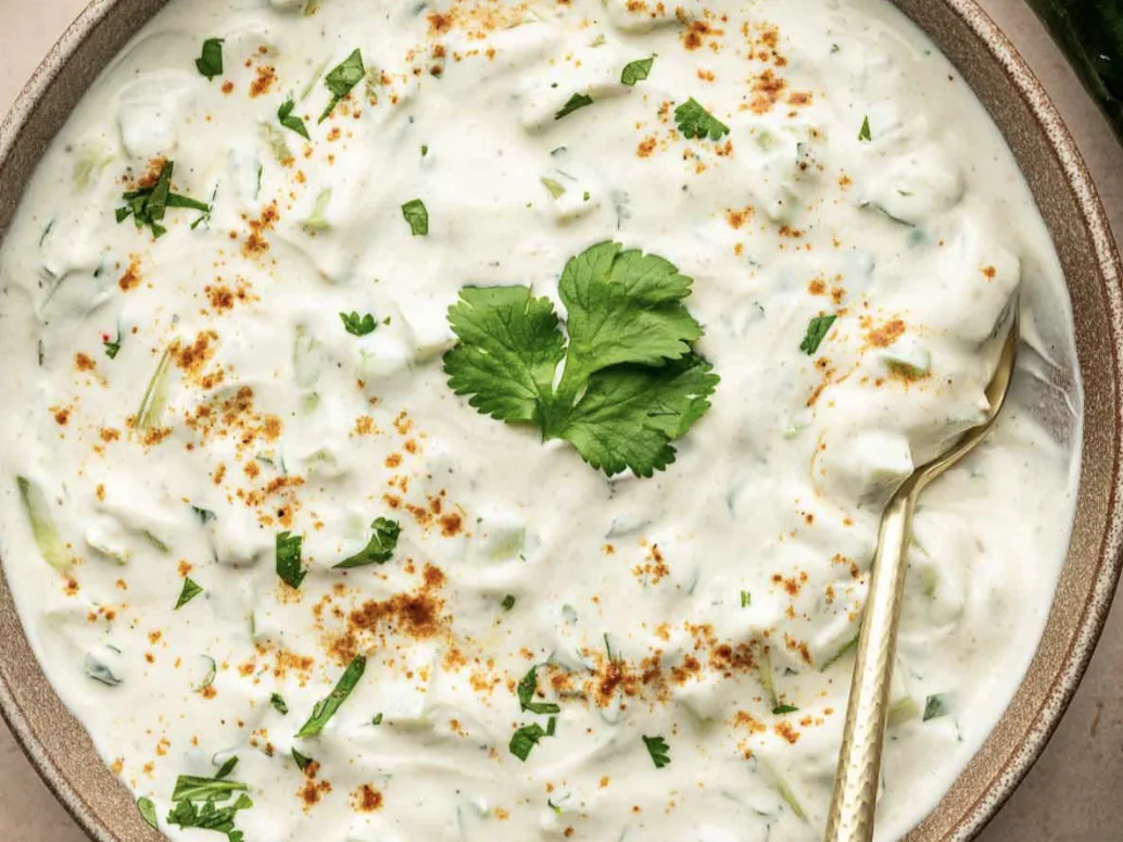 Kachri raita in a stoneware bowl, dusted with roasted spice and topped with cilantro